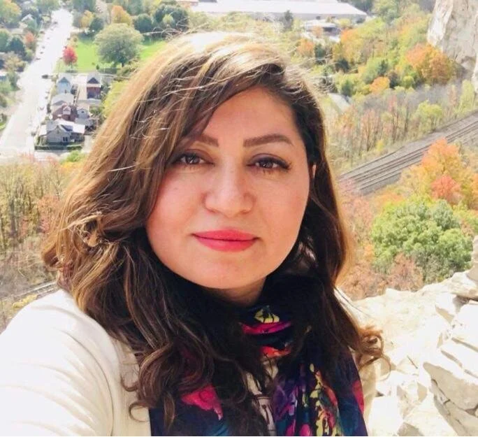 Person taking a selfie on a cliff with a scenic view of autumn foliage and a town in the background.