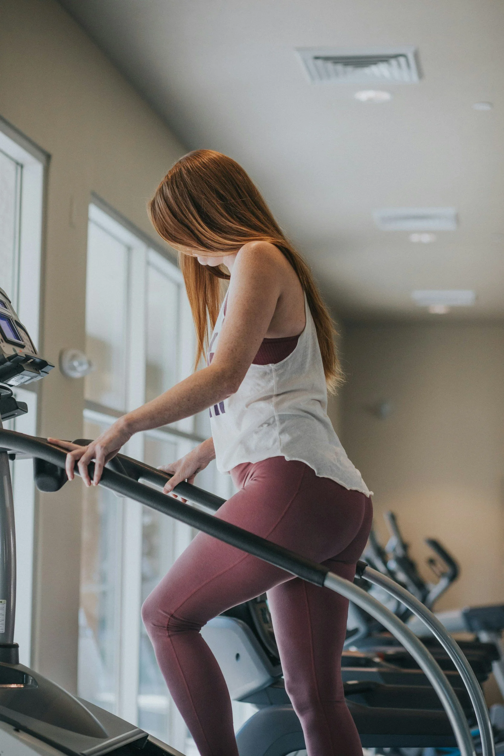 A woman with red hair in workout clothes using a treadmill at the gym.