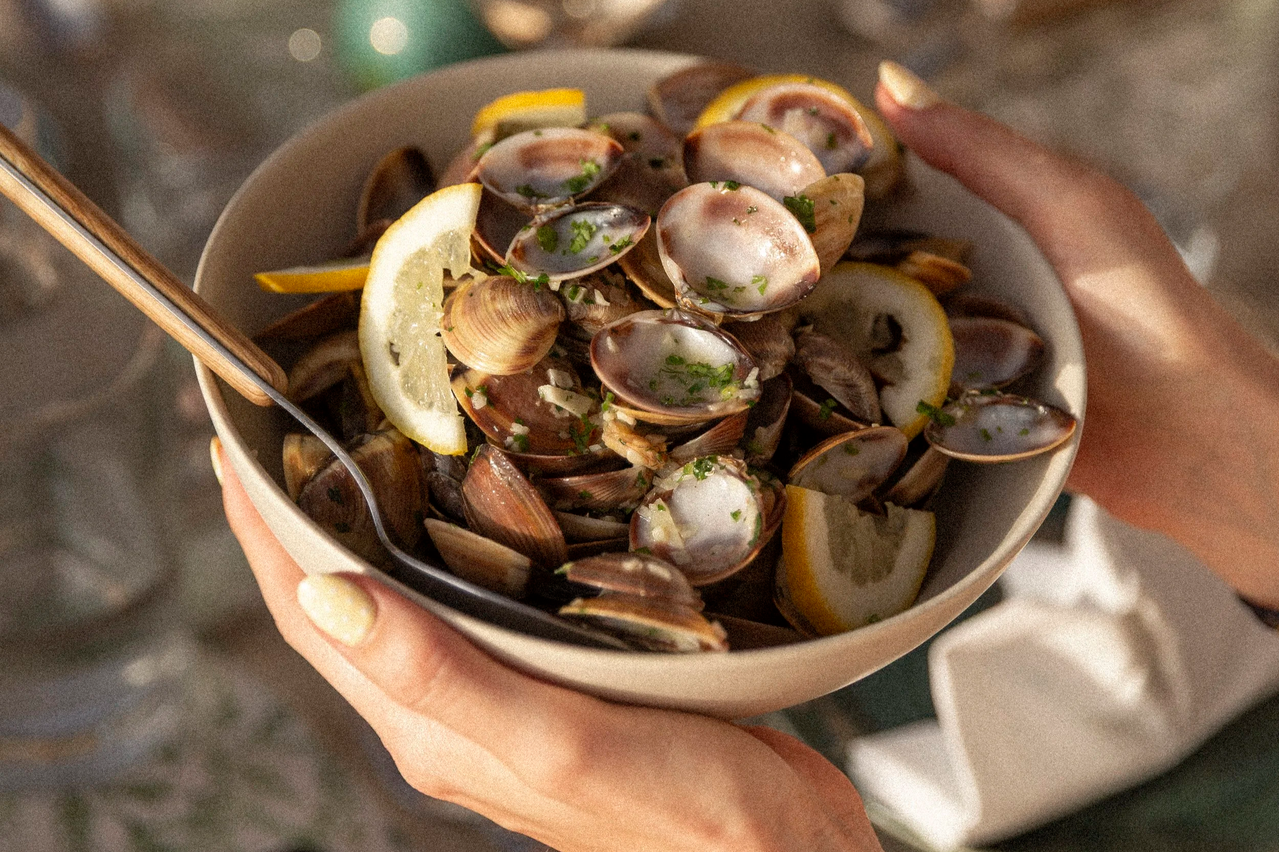 Person hält eine Schüssel mit Muscheln, Zitronenscheiben und Kräutern.