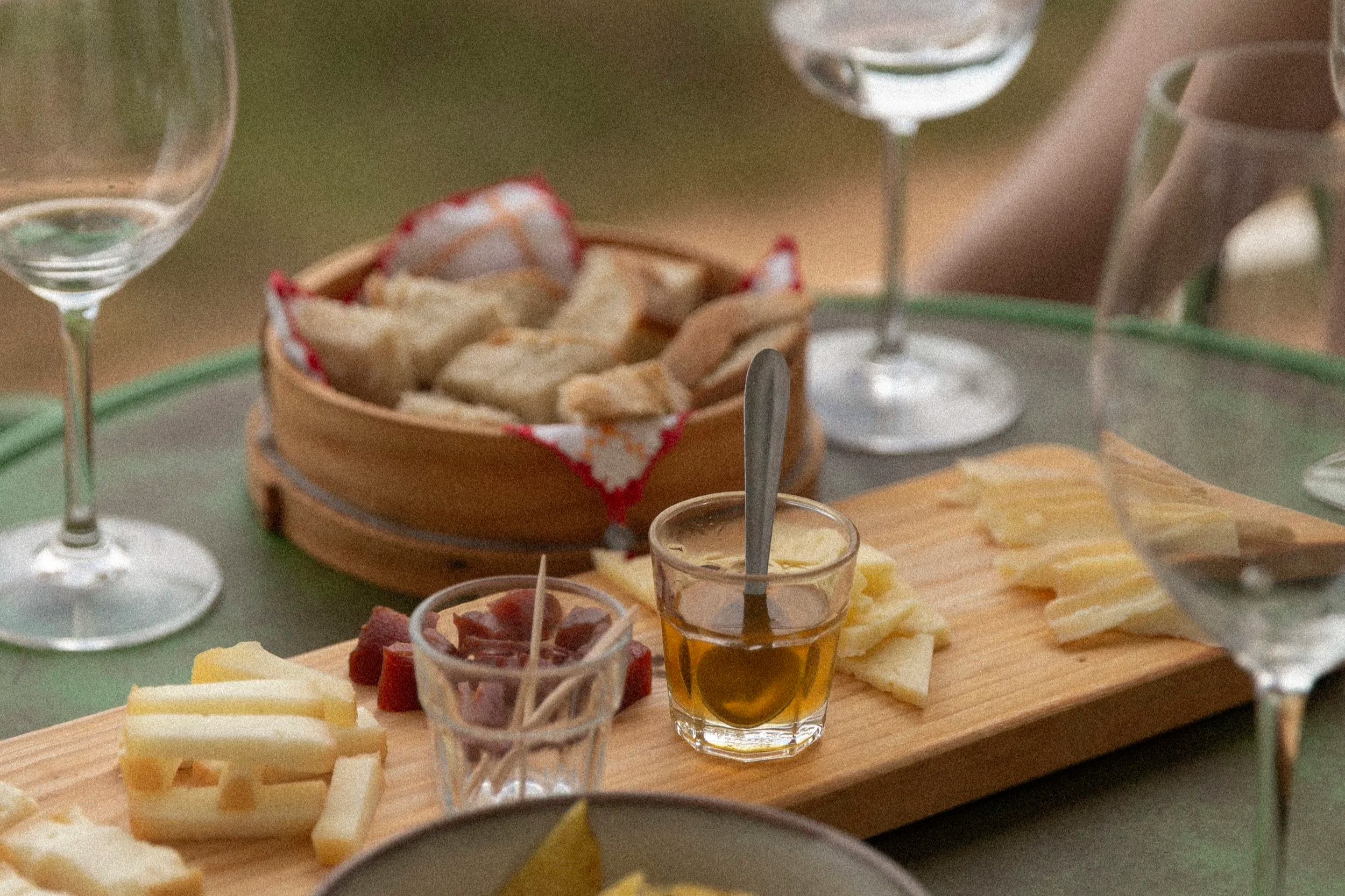 Brett mit Käse, Wurst, Gemüse und passenden Getränken, darunter Wein, auf einem Esstisch.