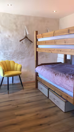 Bedroom with a wooden bunk bed, a yellow chair, and a wall with a hanging hanger.
