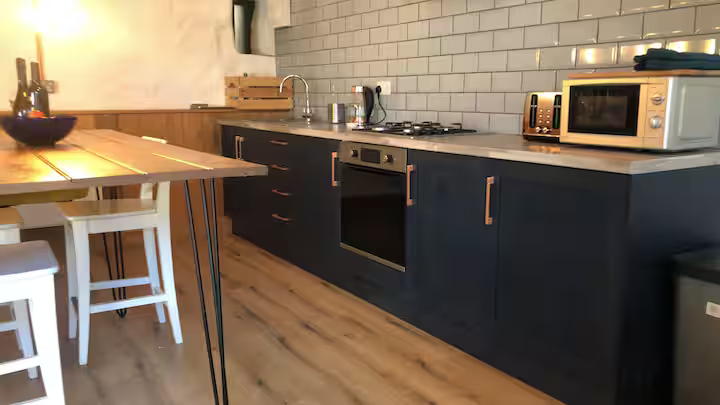 Modern kitchen with dark blue cabinets, white subway tile backsplash, wooden countertop, and small kitchen appliances including a microwave and toaster.