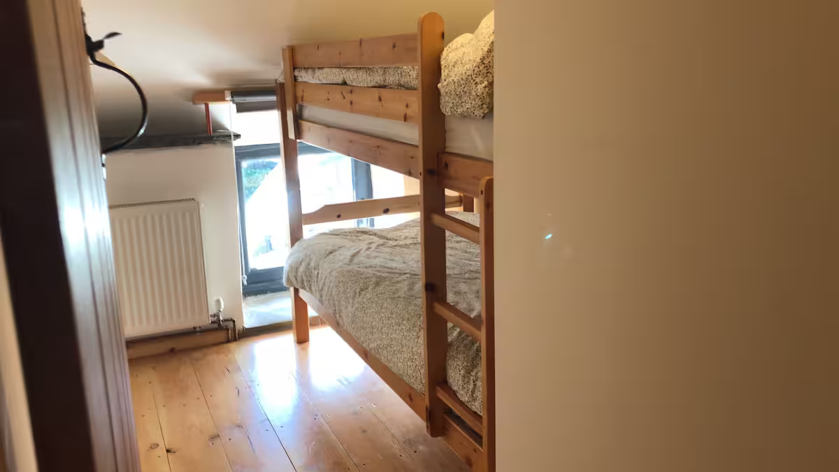 A small bedroom with wooden bunk beds near a window and radiator.