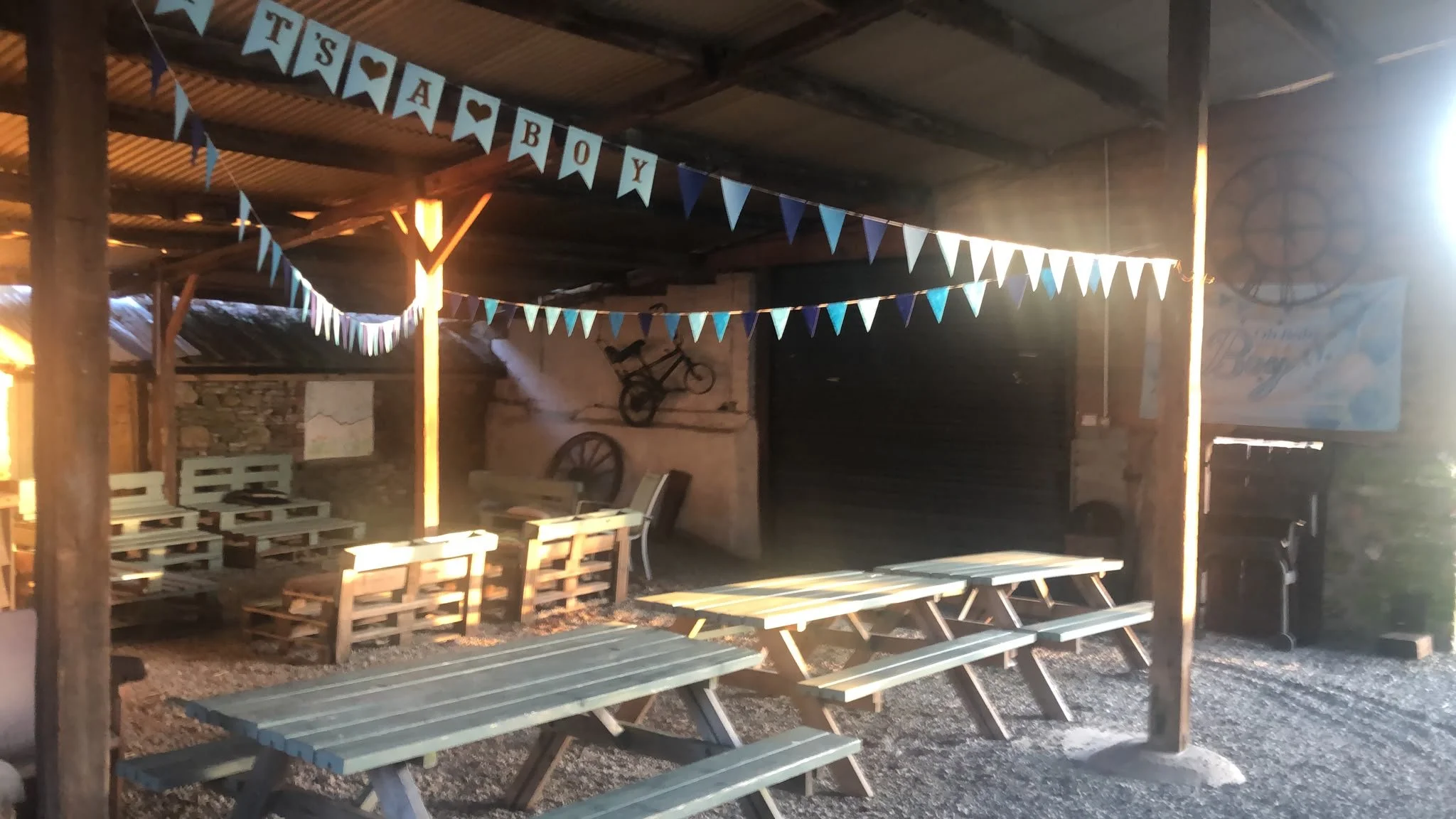 Decorated outdoor seating area at a rustic venue with a banner that says 'It's A Boy' and small tables made from pallets.