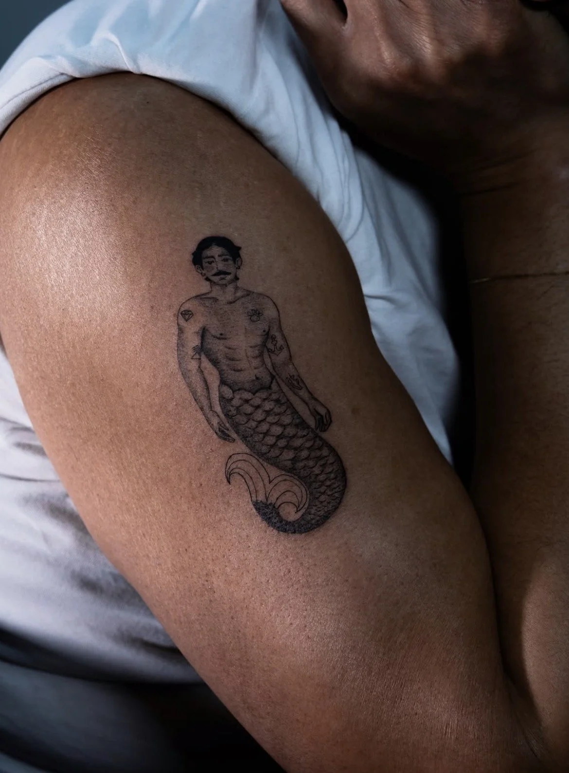 Tattoo of a person with a mustache, upper body muscles, and a fish tail, tattooed on a person's upper arm.