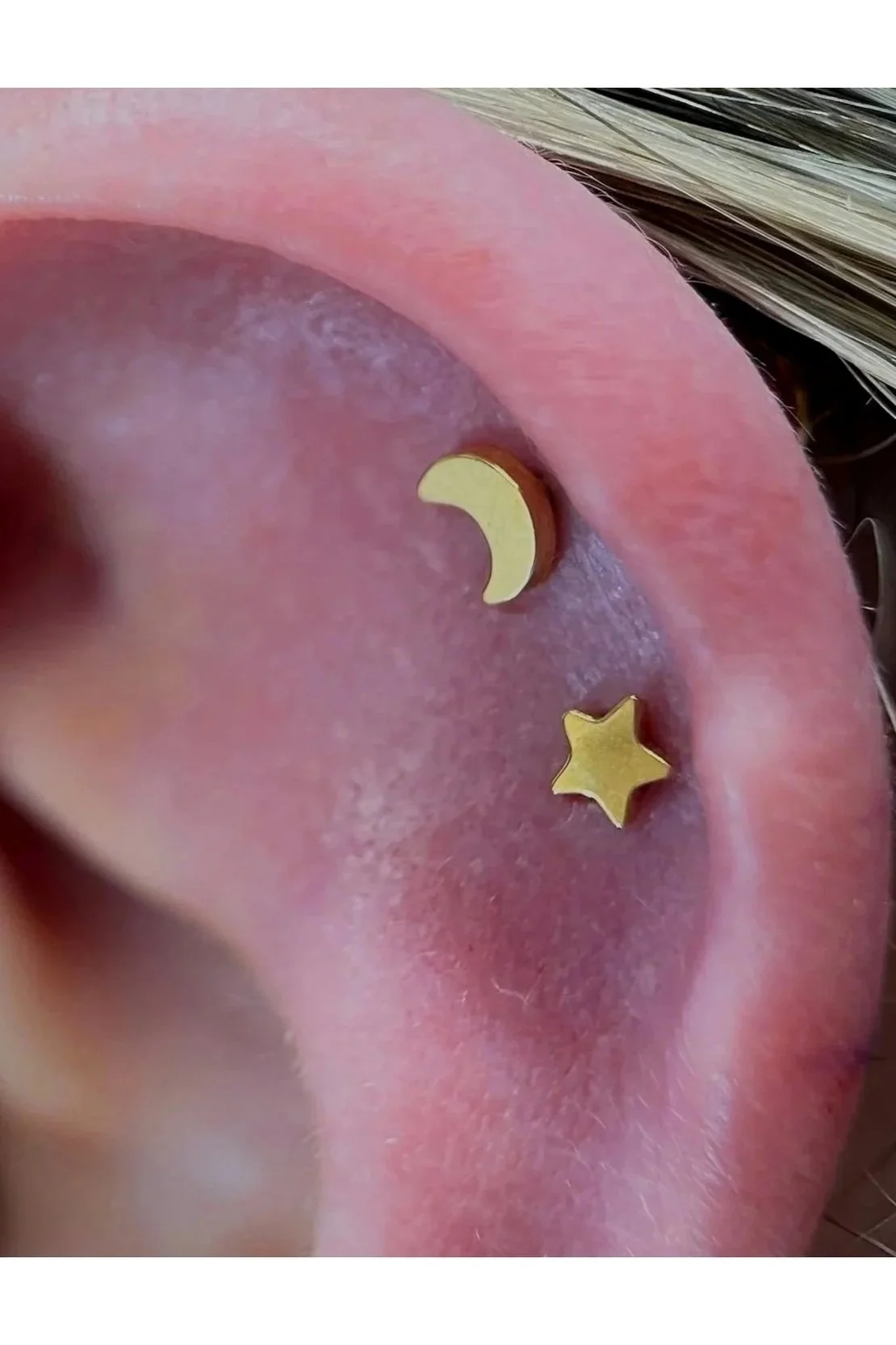 Close-up of a person's ear with a gold crescent moon and star piercing.