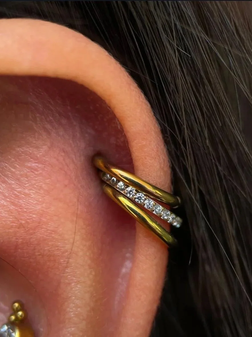 A close-up of a human ear with two gold rings, one with diamonds, stretched in the earlobe, revealing skin and dark hair.