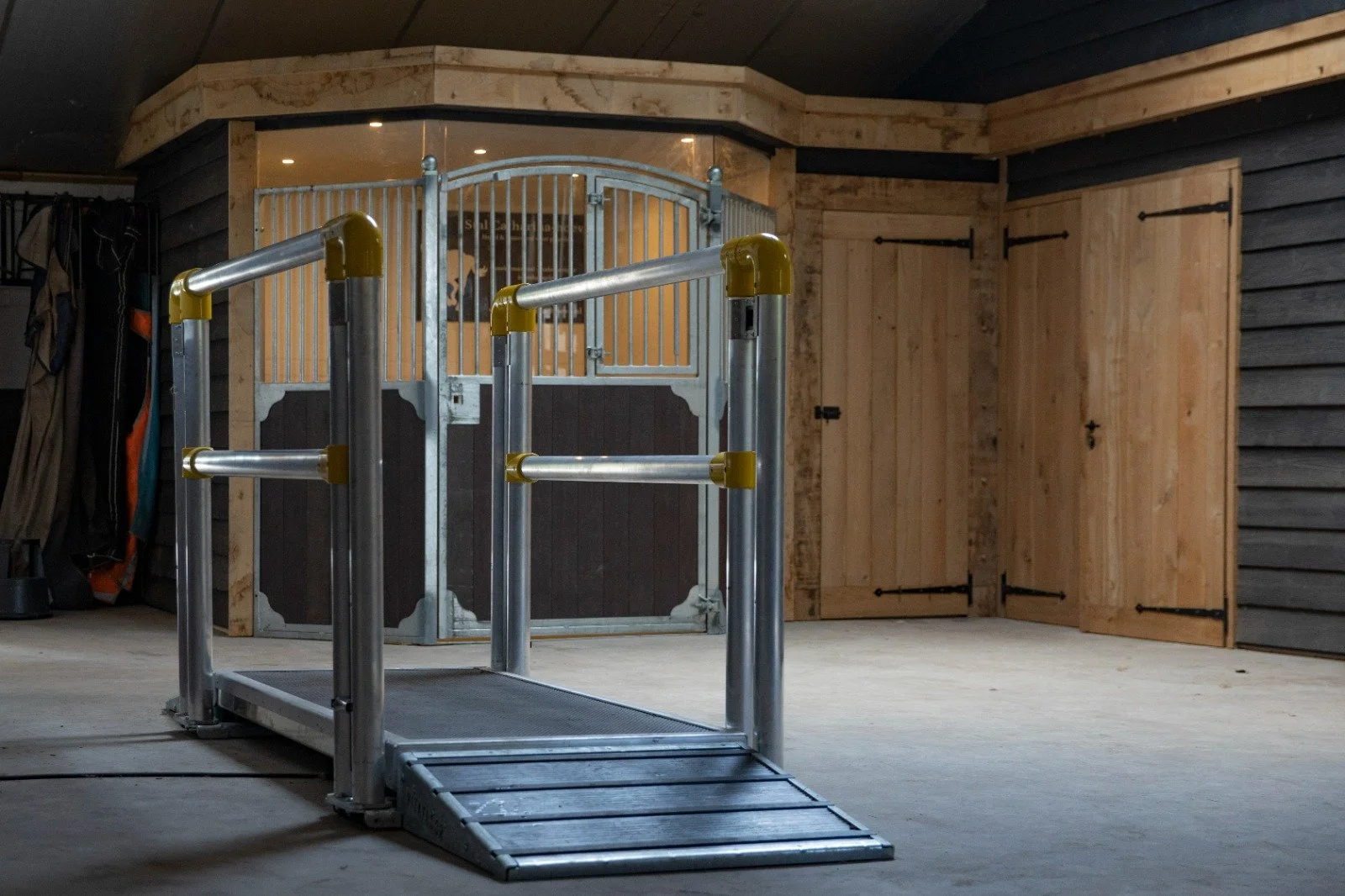 Indoor equestrian riding arena with a metallic, blue, wheelchair accessible ramp leading to a round pen with wooden doors and walls.