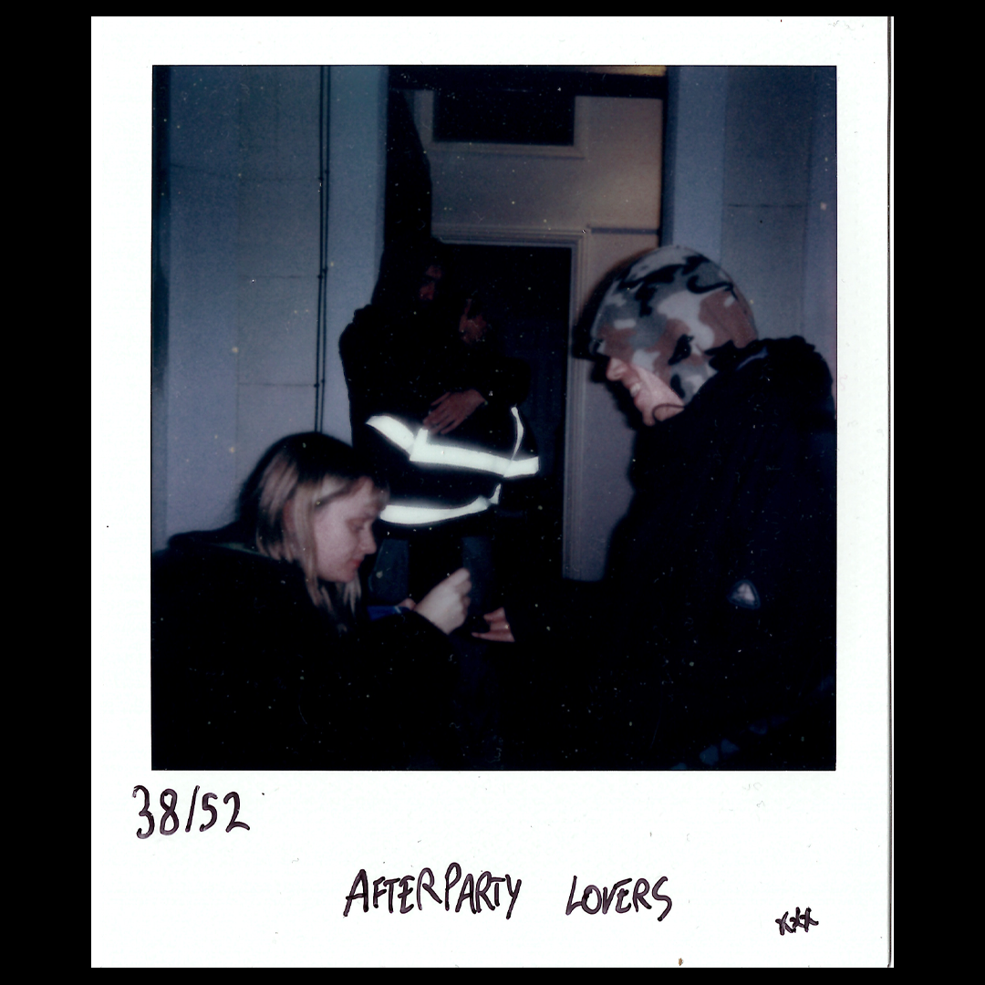 A woman with long hair looking at her phone, a man wearing a camouflage helmet and black jacket facing her, and two people in the background reflected in a mirror. Text on the photo reads "38/52 AFTERPARTY LOVERS".