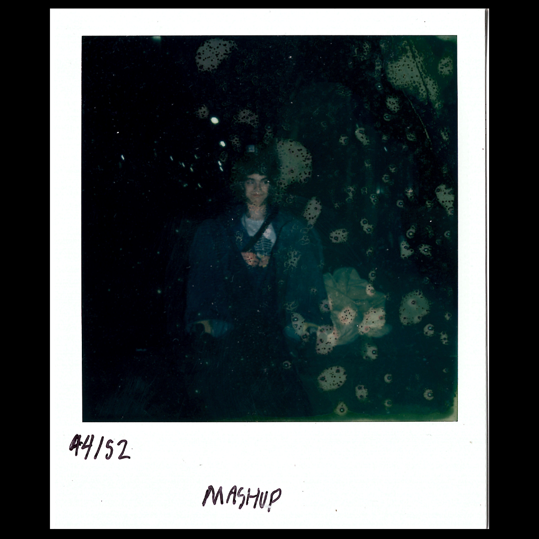A woman in a dark coat standing in front of a window covered in soap bubbles or foam, with a reflection of her face visible in the glass.