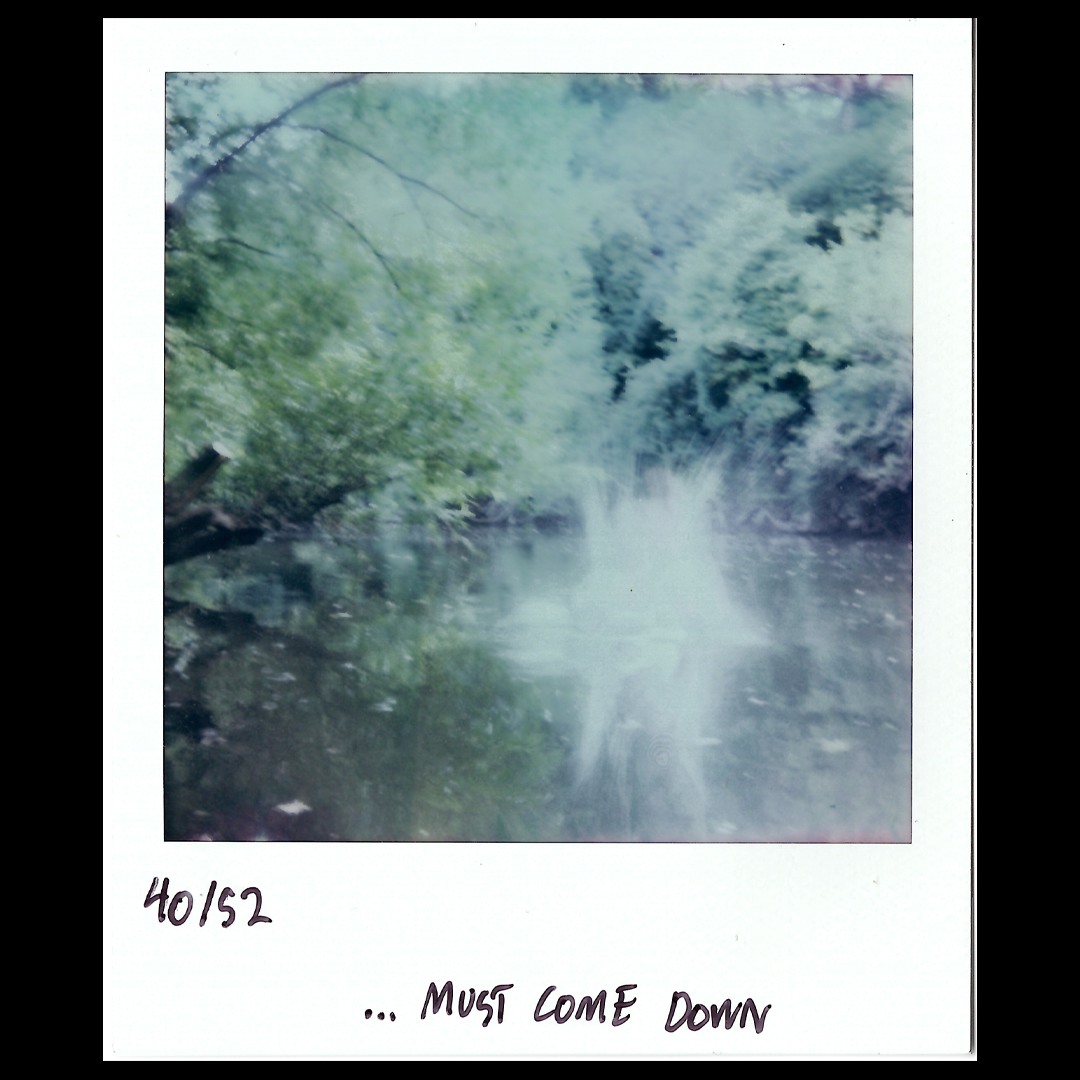 A blurry nature scene of a stream surrounded by green trees with the hand-written note '40152 ... Must Come Down' at the bottom.
