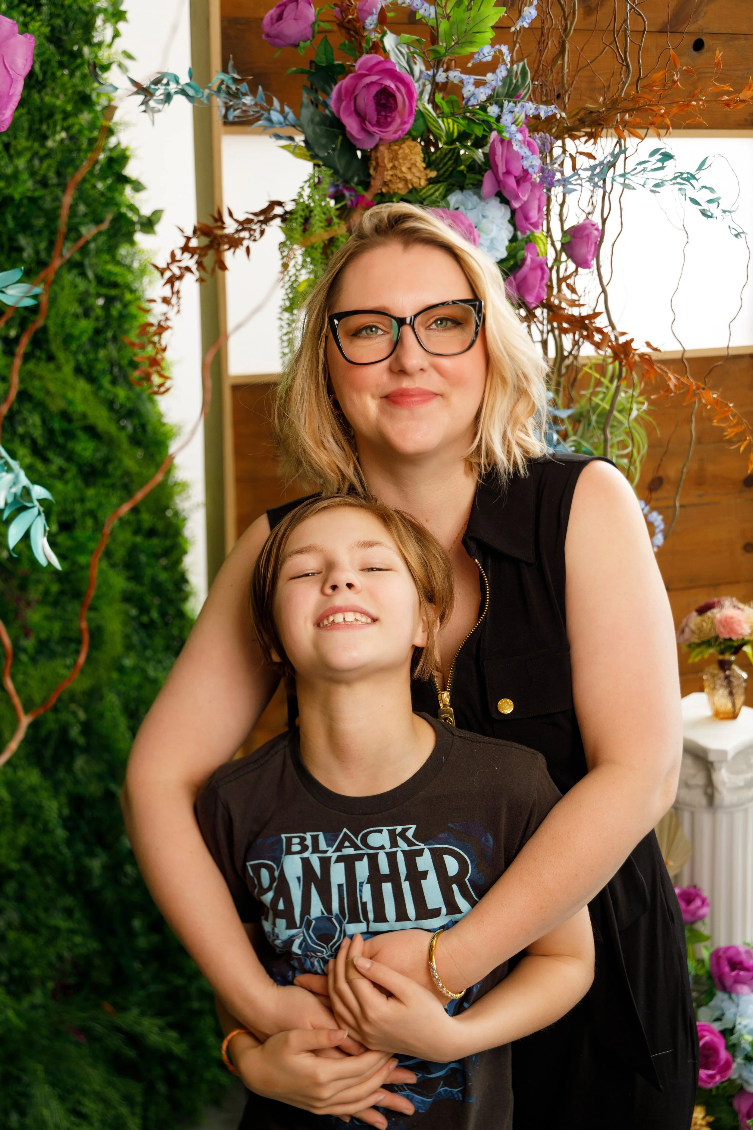 A woman and a young child in a floral setting, smiling and hugging.