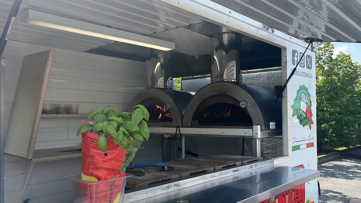 Un camion-restaurant avec deux fours à pizza en fonctionnement et un pot de basilic frais.