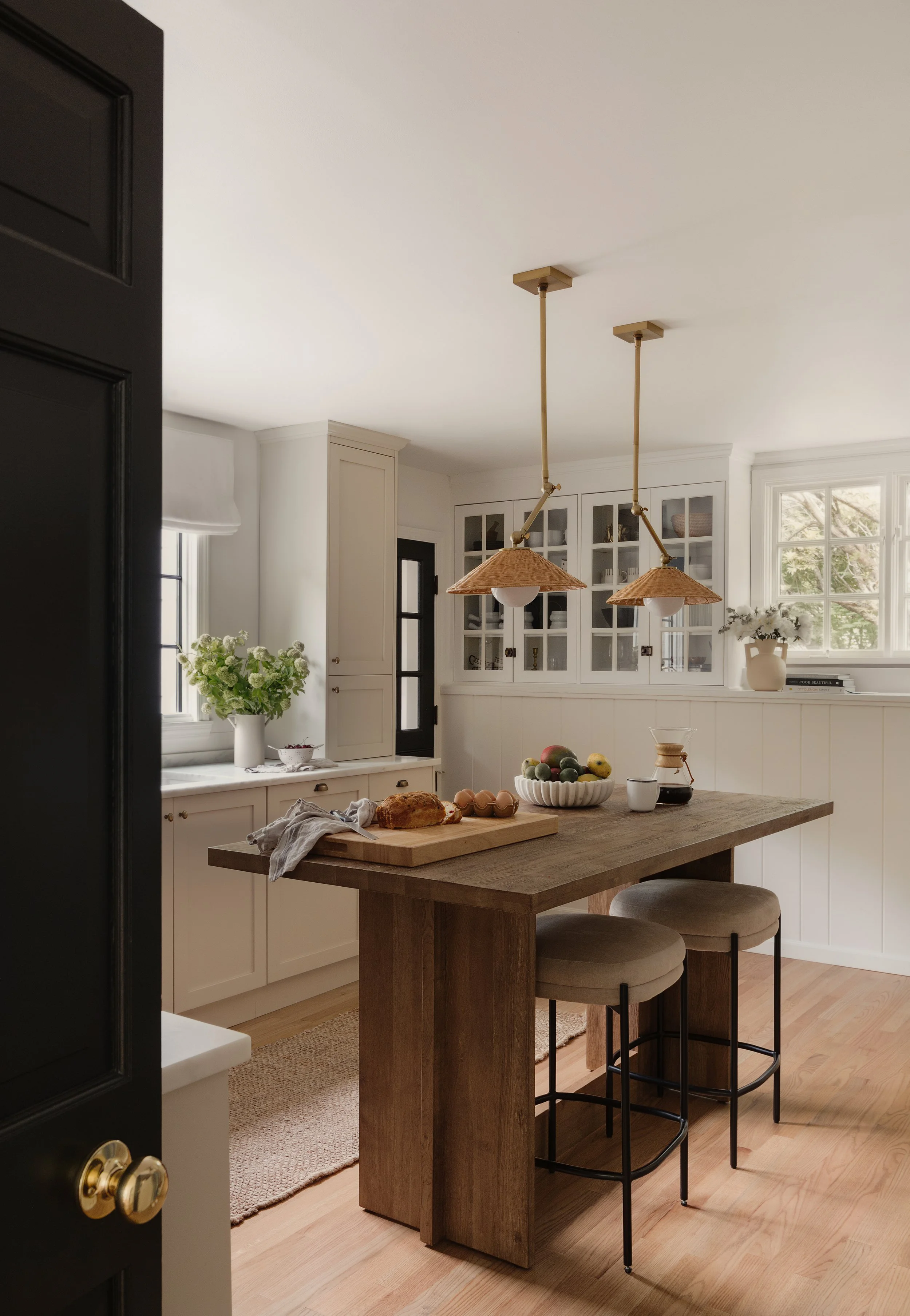 Remodeled kitchen with white cabinets, a wood island, two barstools, fruit bowl, and pendant lights.