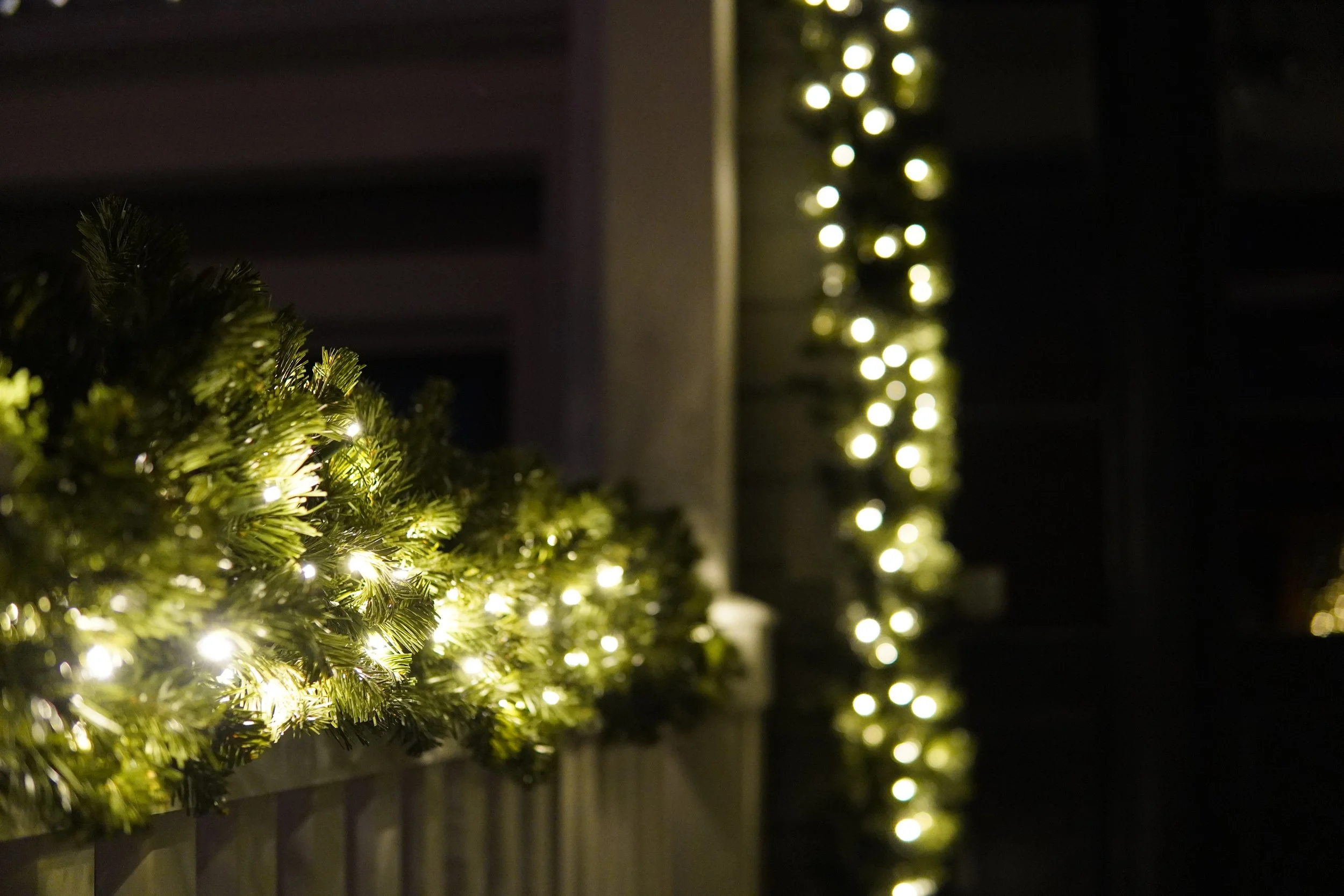 Close-up of a green garland with white string lights, with additional lights visible in the background, creating a festive atmosphere.