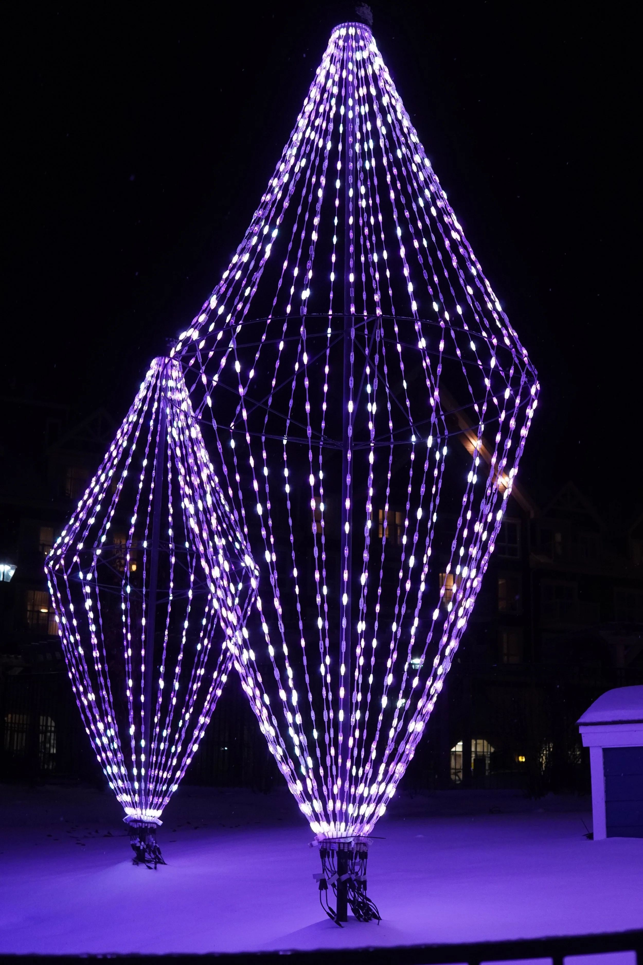 A large, illuminated purple and white light display shaped like a diamond, set against a dark night sky.