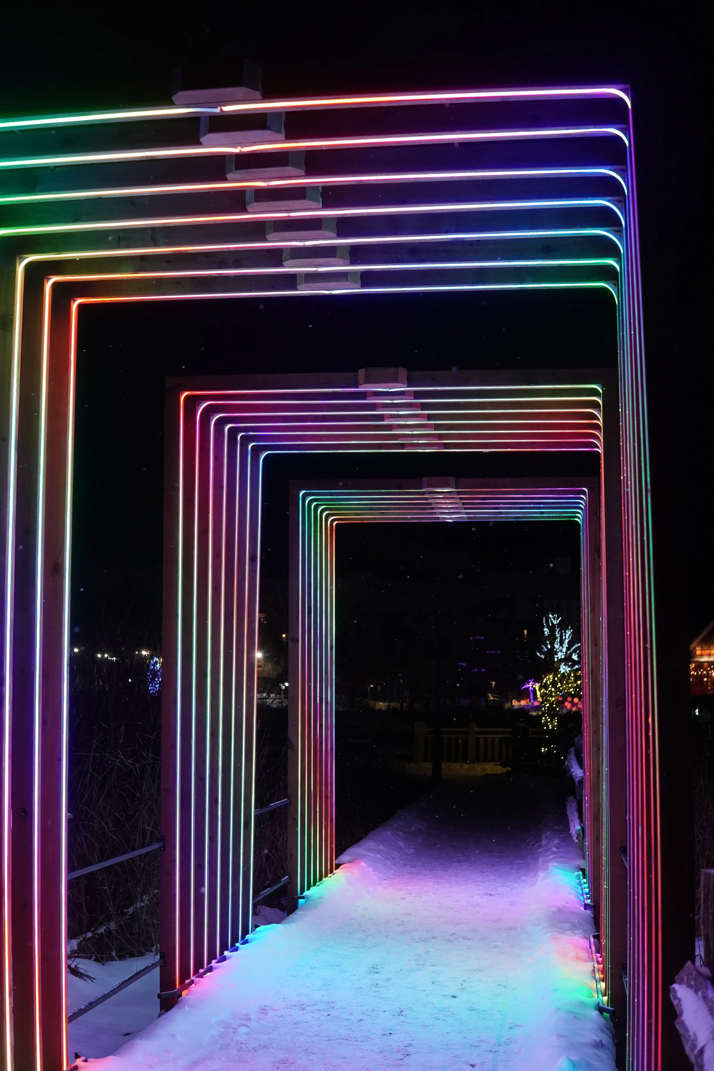 Colorful neon light archways over a snowy pathway at night.