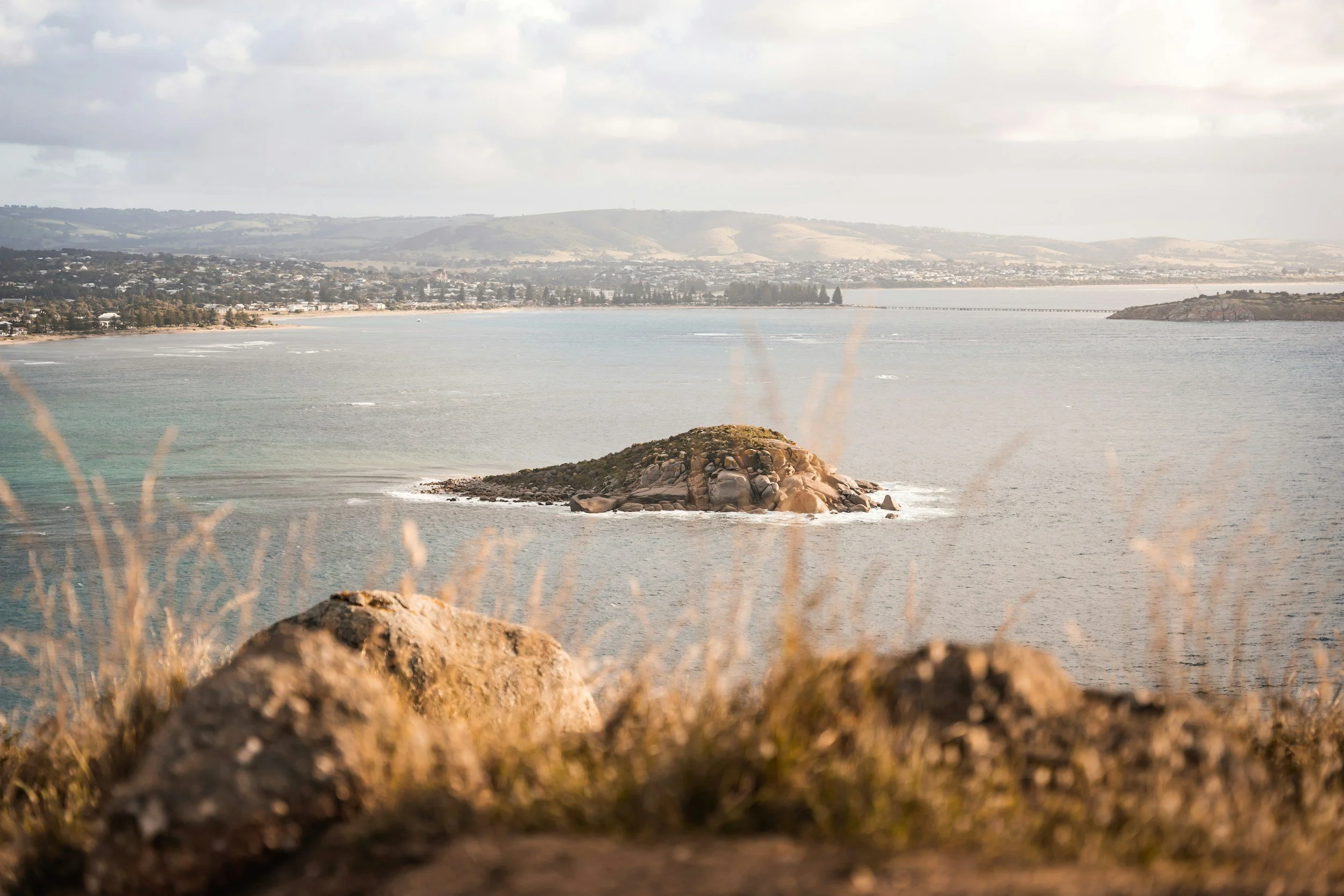 A scenic view of the ocean from a hill, showcasing the vast water and distant horizon under a clear sky.
