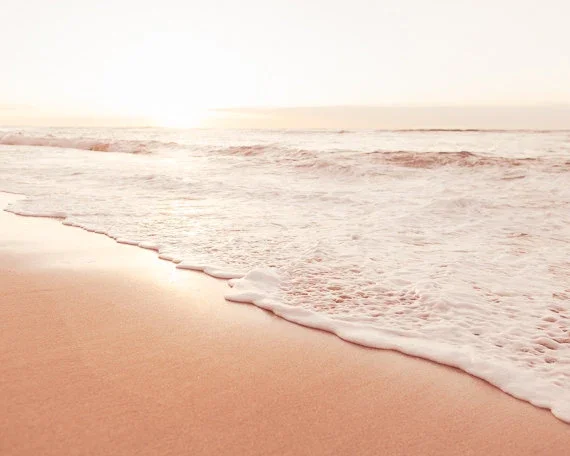 A serene beach at sunset, with gentle waves lapping against the golden sand under a colorful sky.