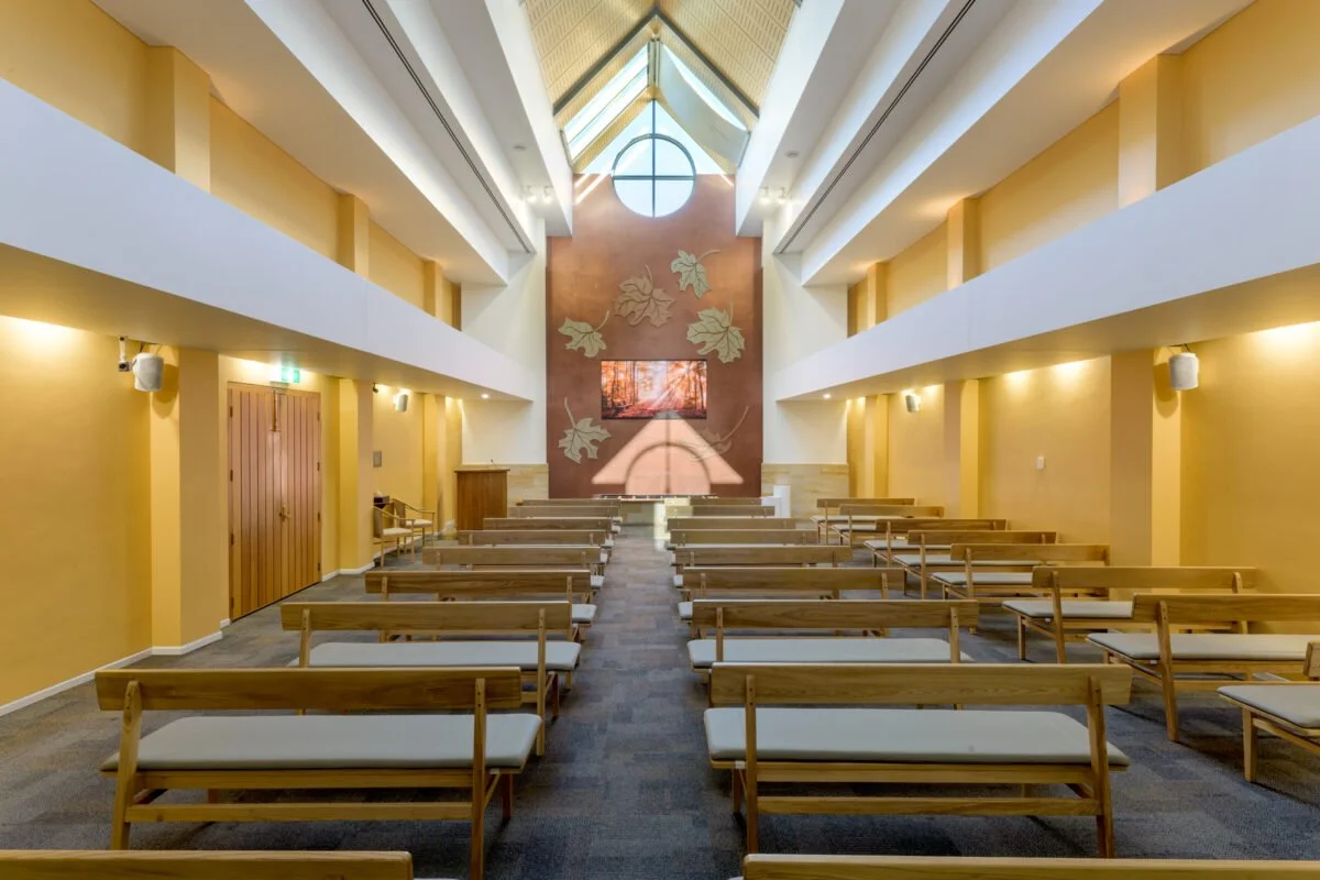 A church interior featuring wooden benches and a large screen for presentations or services