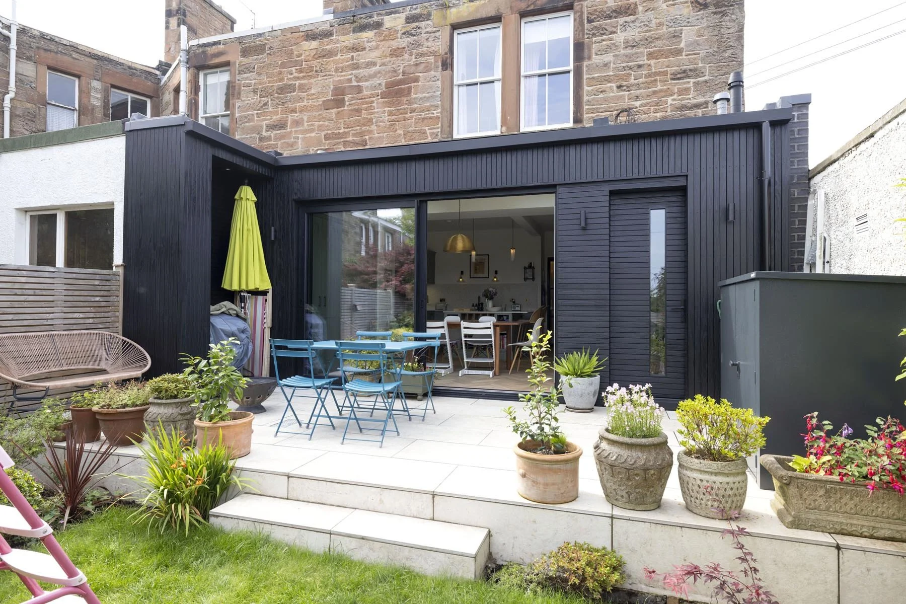 black aluminium sliding doors to rear extension in morningside edinburgh with large porcelain patio and green umbrella designed by edinburgh architect