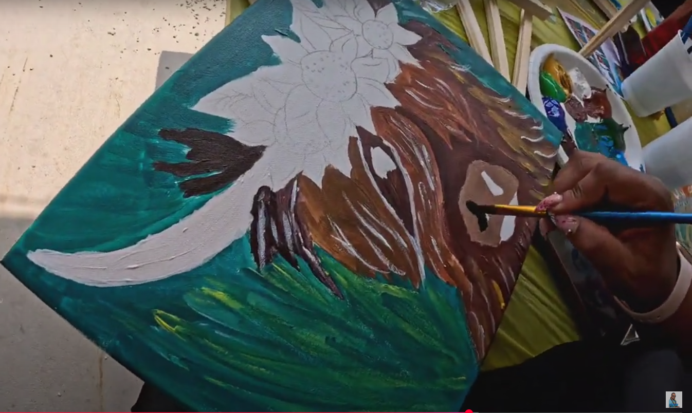 Person painting an acrylic or oil canvas with a floral design, featuring a white flower with brown and yellow accents and a green background.