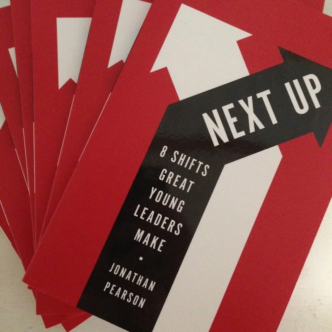 Brochure or flyer with a red background, featuring a white arrow with a black banner that says "NEXT UP" and text mentioning "8 shifts, great young leaders, make" by Jonathan Pearson.