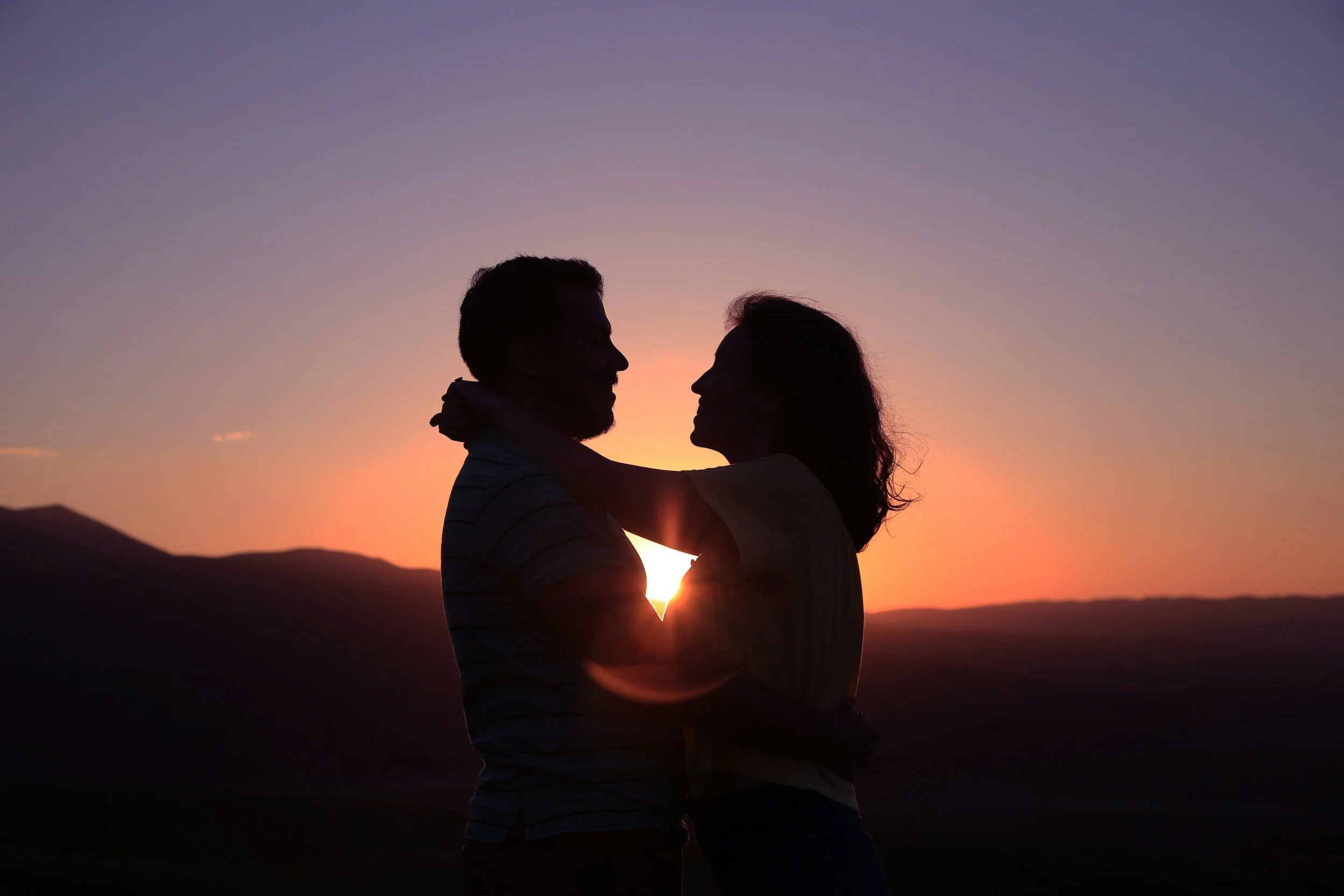 A silhouette of a couple embracing during sunset over mountains.