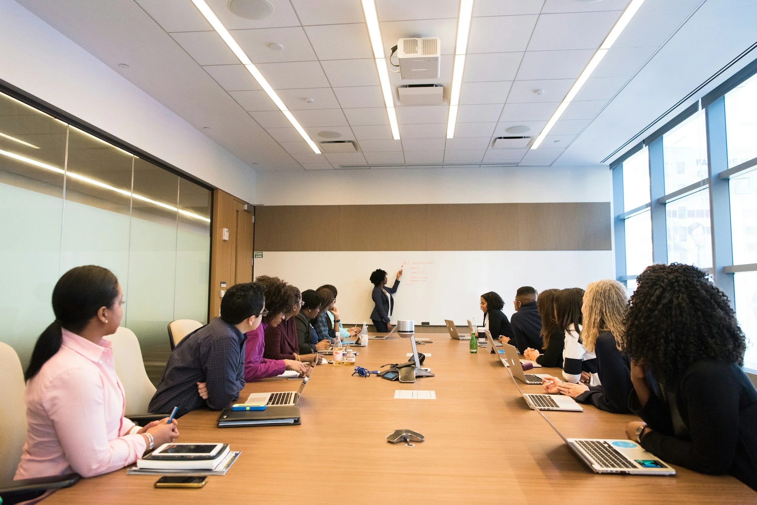 Facilitator leading a diverse team in an interactive workshop, guiding organizational learning and strategy on a whiteboard in a modern conference room.
