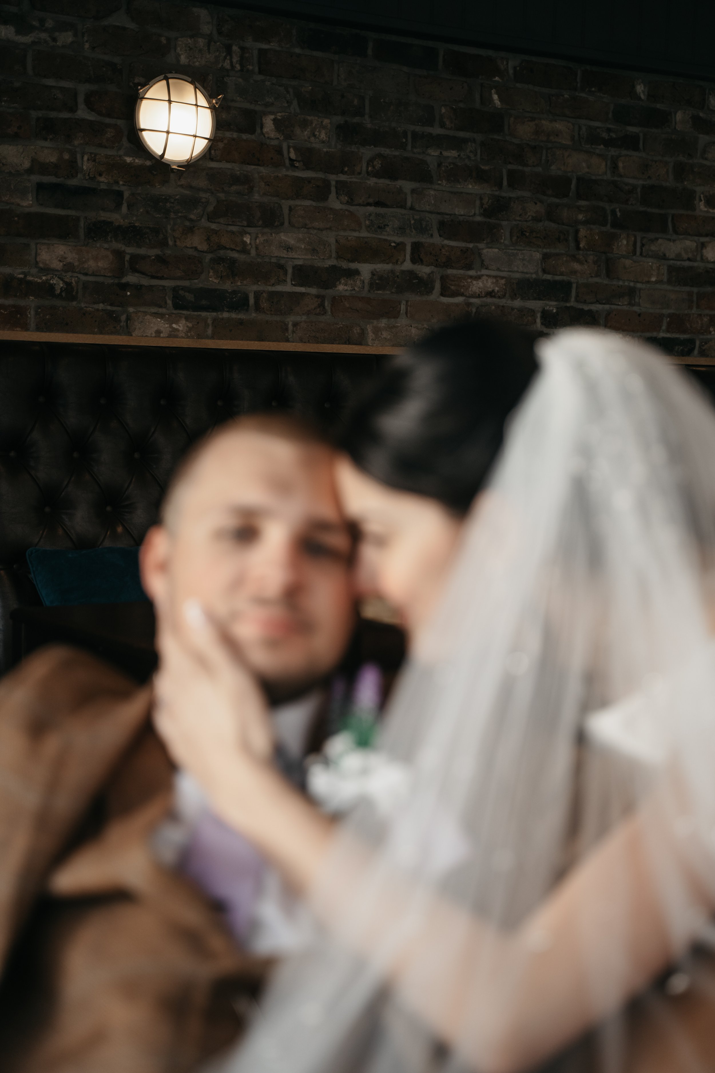 Blurred image of two women in a restaurant or cafe, with a brick wall and industrial-style light fixture in the background.