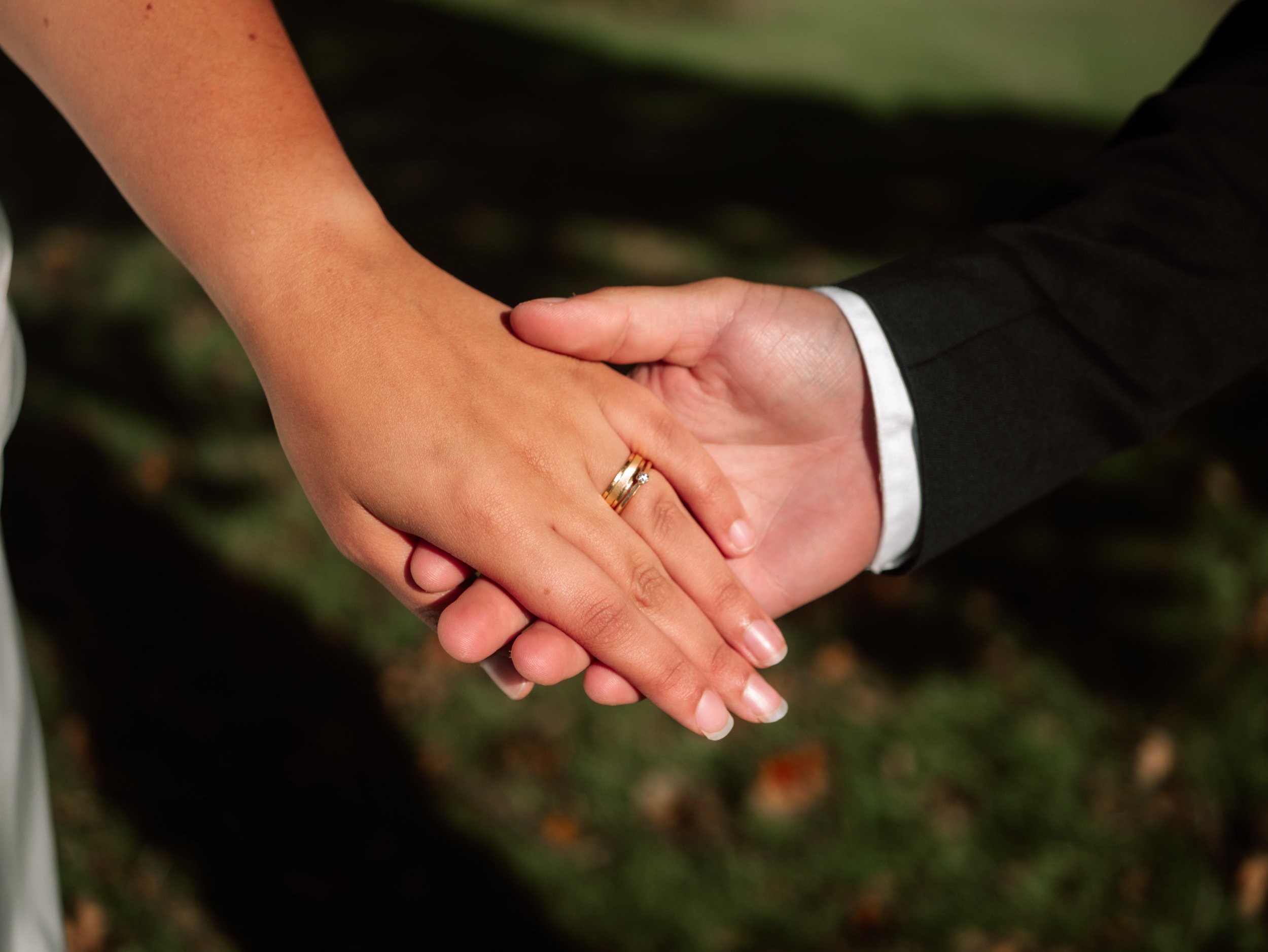 A close-up of a bride and groom holding hands, with wedding rings visible, during a wedding ceremony.