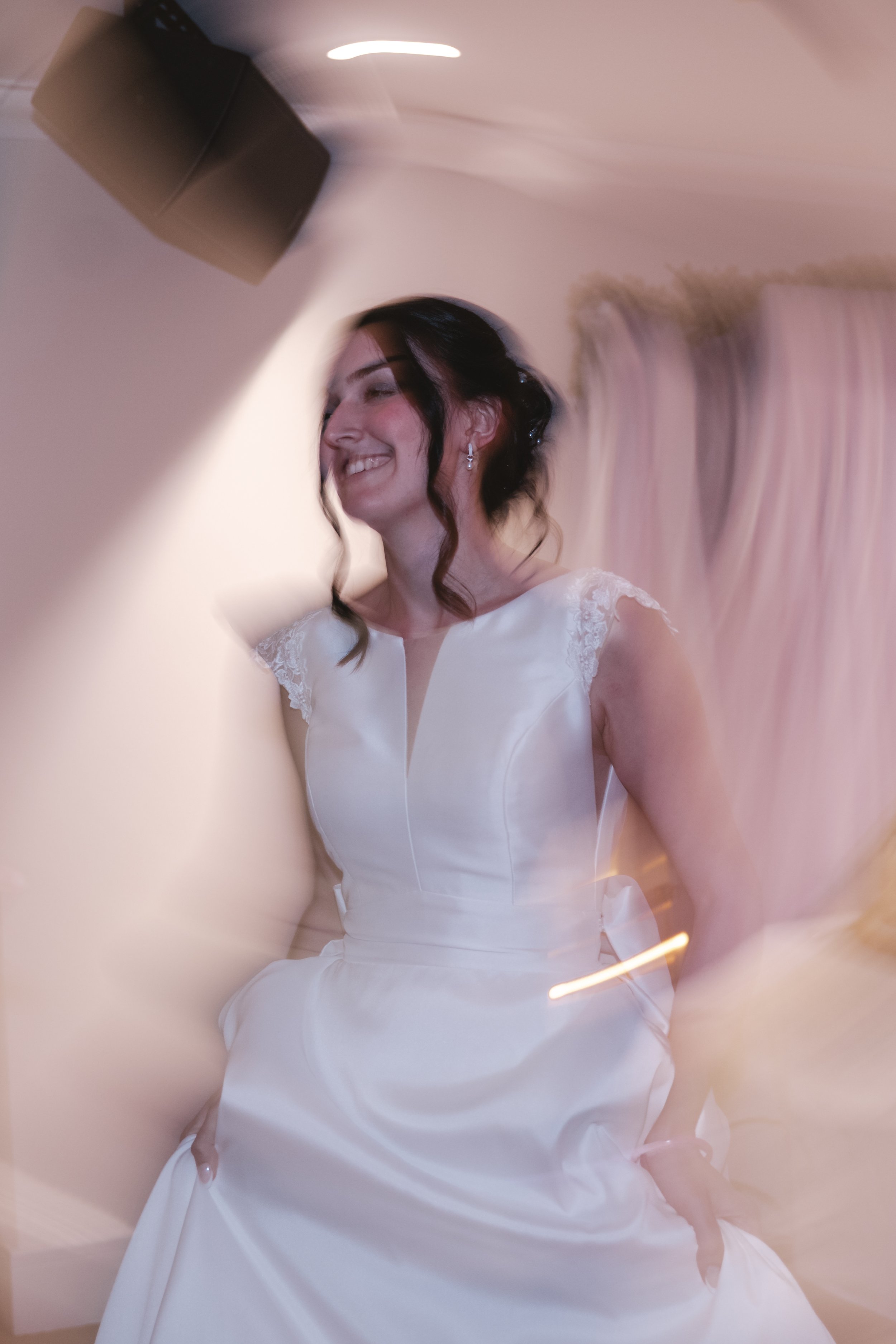 A woman in a white dress smiling, with a distorted and blurred background caused by the camera effect.