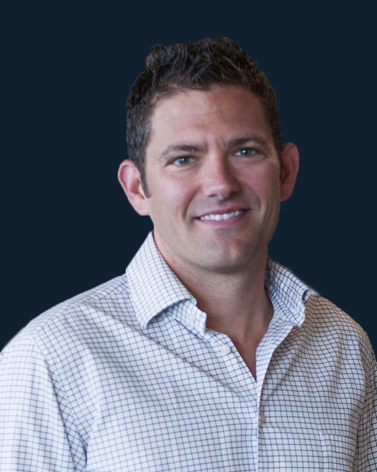 A smiling man with short, dark, curly hair, wearing a white checkered shirt against a dark background.