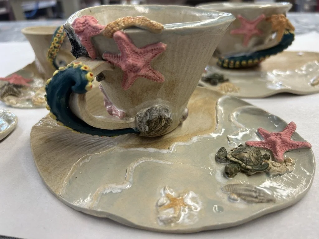 Decorative ceramic teacup and saucer set with beach-themed embellishments, featuring starfish, turtles, and seashells.