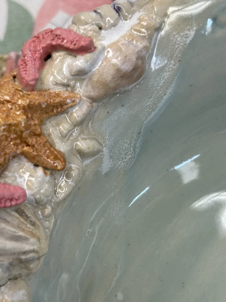 Close-up of a ceramic sea-themed design with a starfish, sea shell, and coral detailing on a glossy surface.