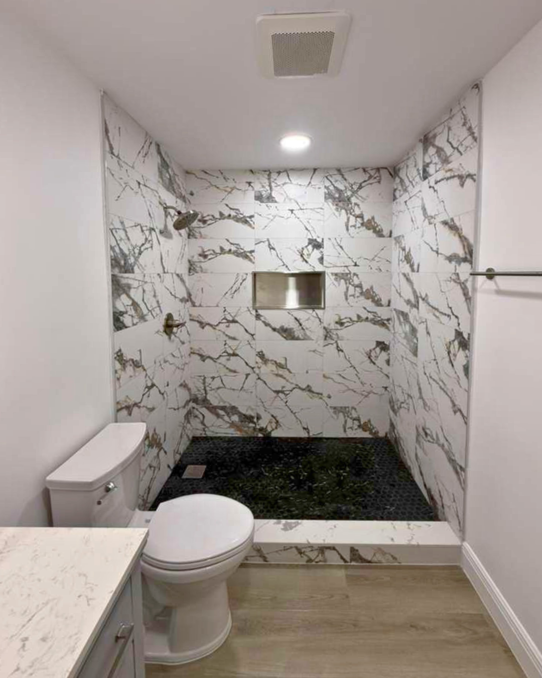 The new walk-in shower became the centerpiece of the bathroom, featuring marble-look tile, a custom niche, and pebble flooring