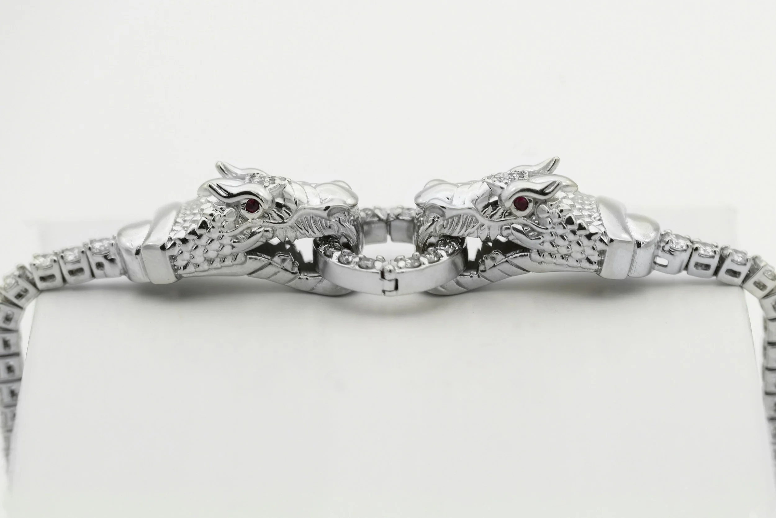 Silver bracelet with two dragon head designs facing each other and a clasp in the middle, placed on a white surface.