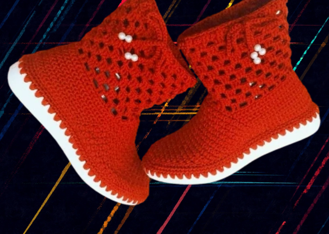 Red knitted crochet shoes with white soles placed on a colorful checkered fabric background.