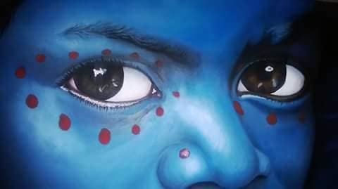 Close-up of a face painted blue with red dots around the eyes, depicting a fantastical or cultural theme.