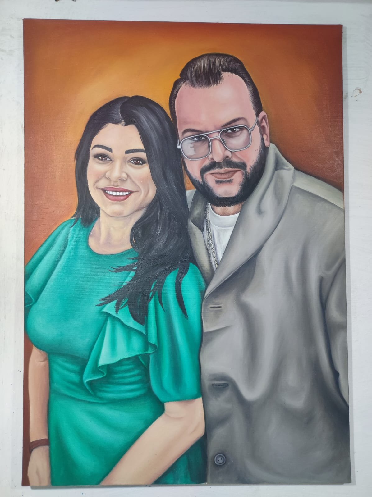 Portrait painting of a woman with long black hair in a green dress and a man with short hair, beard, glasses, and a gray coat against an orange background.