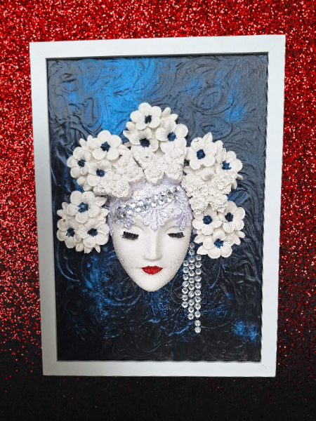 Decorative mask artwork featuring a white mask with red lips, adorned with white flowers and blue accents, set against a textured blue background, inside a white frame, on a red glittering surface.