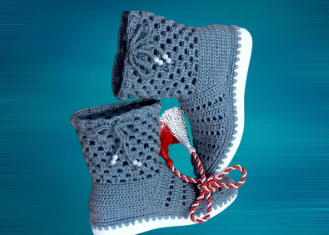 Gray knitted baby boots with red and white striped laces, set against a blue background.