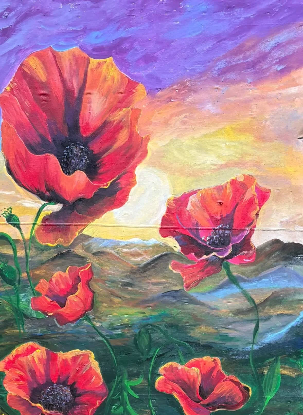 A colorful painting of red poppies blooming in a field during sunset, with a vibrant sky in shades of purple, pink, yellow, and blue.