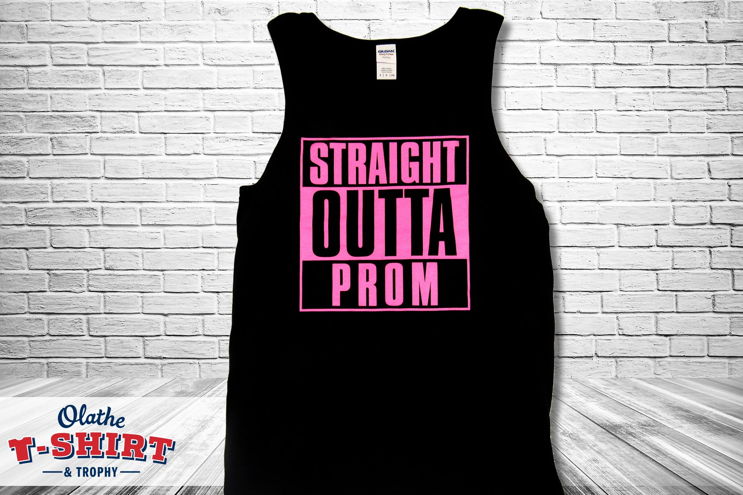 Black sleeveless T-shirt with pink text that reads 'STRAIGHT OUTTA PROM' hanging against a white brick wall.