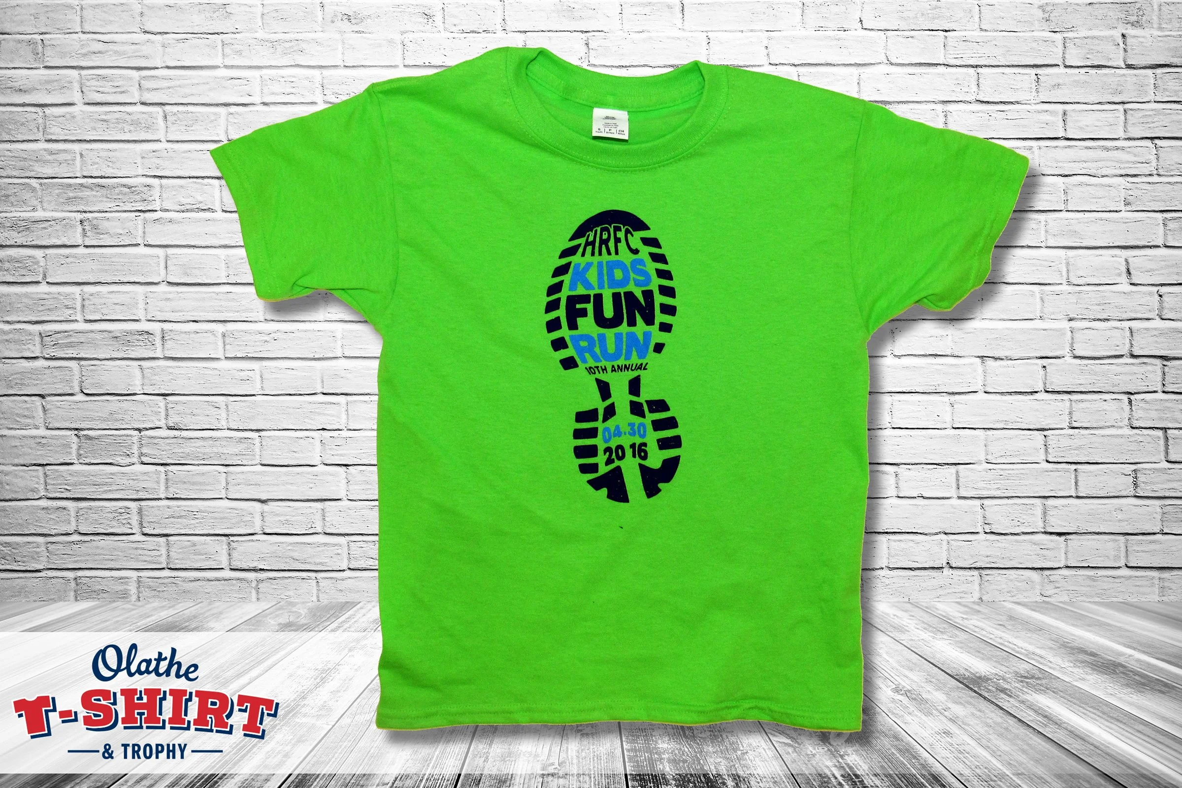 Bright green t-shirt with a black and blue running shoe print, the shoe outline contains the words 'HRFC Kids Fun Run 10th Annual 04.30 2016'.