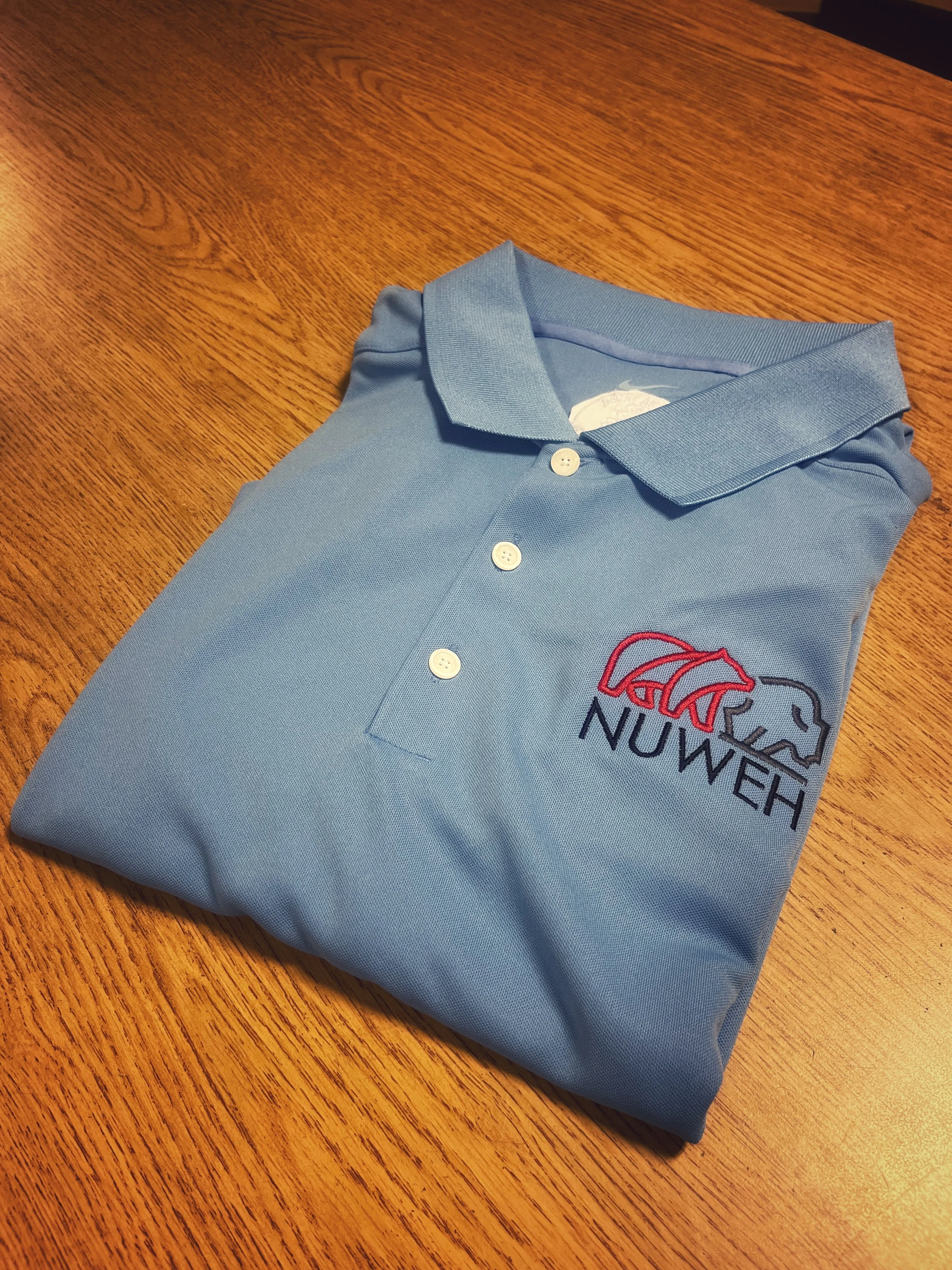 Folded light blue polo shirt with an embroidered chest logo.