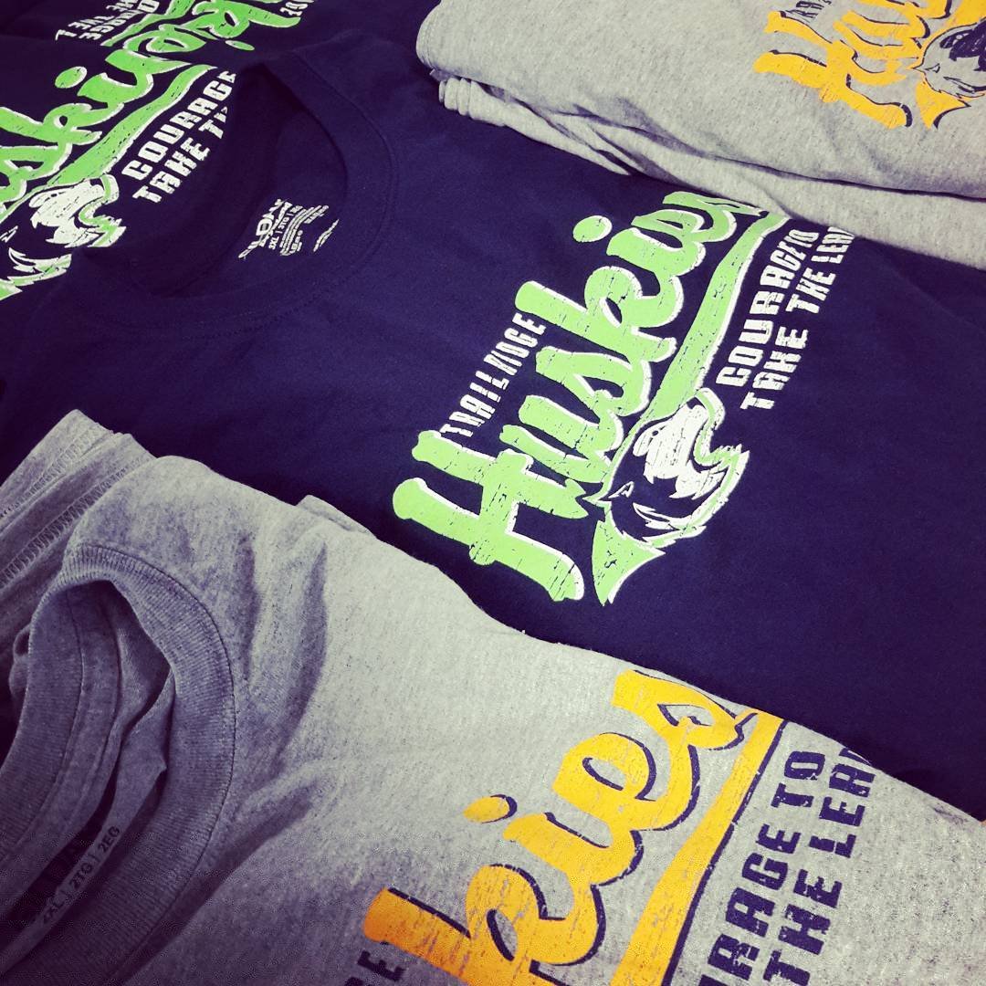 Stacked black and gray shirts with printed logos and slogans.