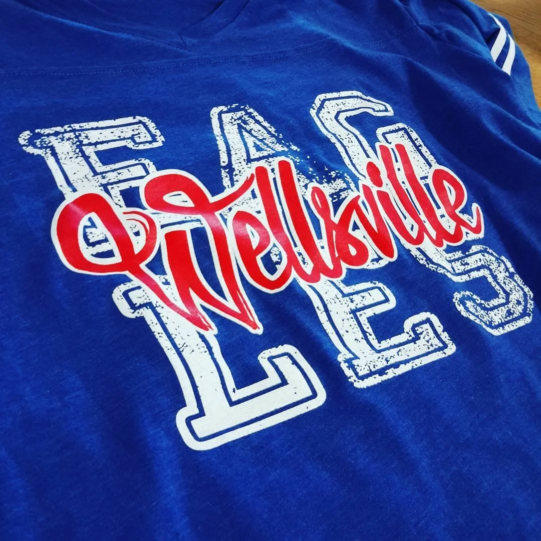 Blue T-shirt with large white outlined letters and red script.