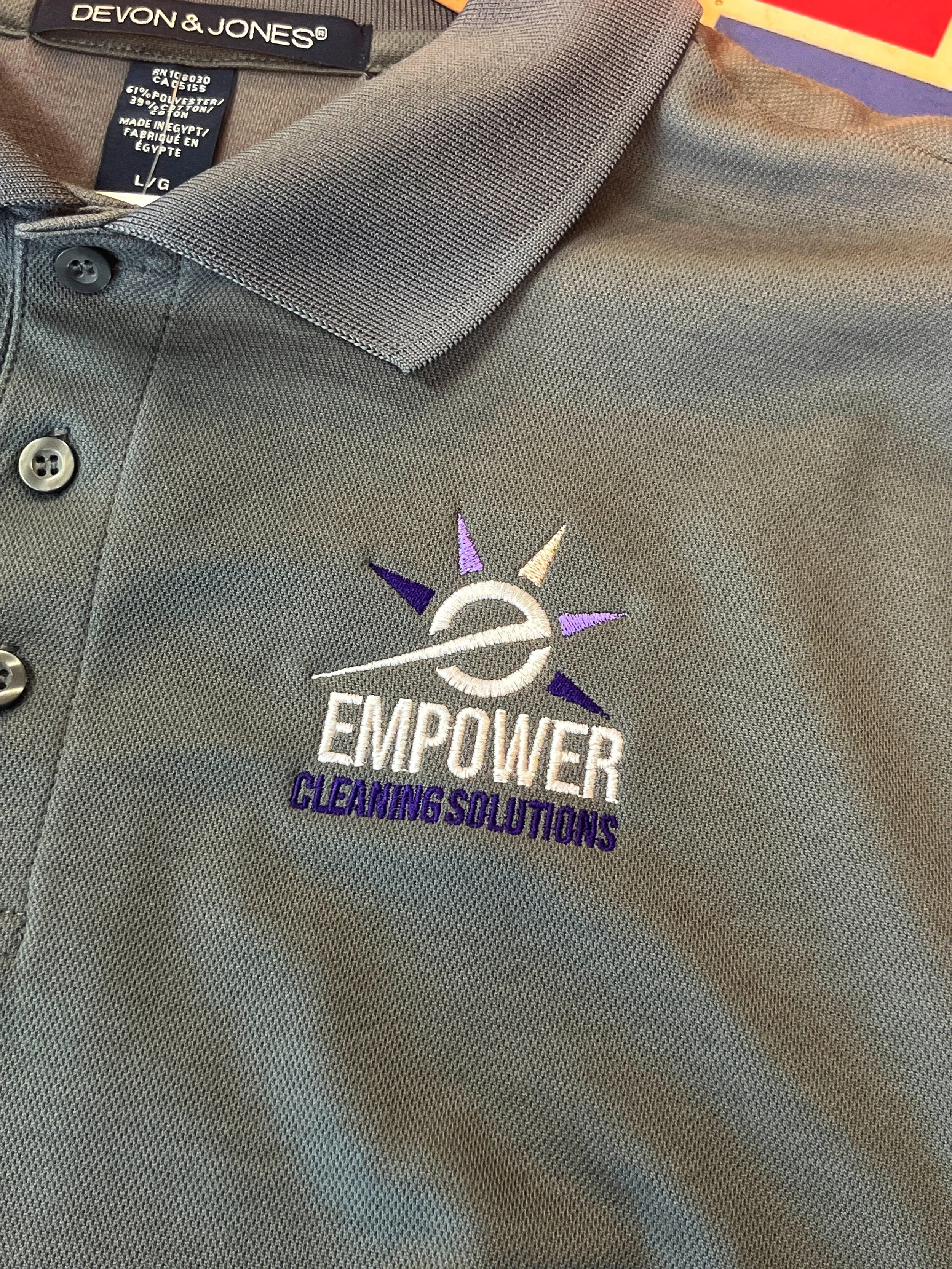 Gray polo shirt with embroidered logo for Empower Cleaning Solutions, featuring a compass and sun design, with black buttons and a Devon & Jones label.