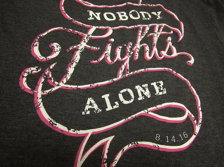 Text on a dark fabric that reads 'Nobody fights alone' with a date '8.14.16' at the bottom.